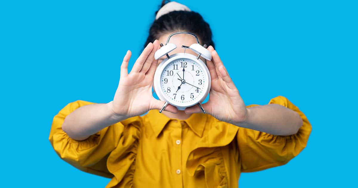 Woman holding white alarm clock in front of her face