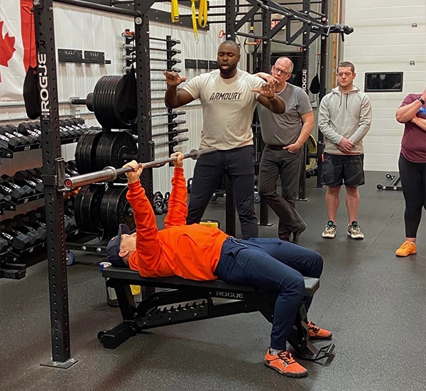 Matt laying on the bench press demonstrating proper form with Lee Boyce speaking 